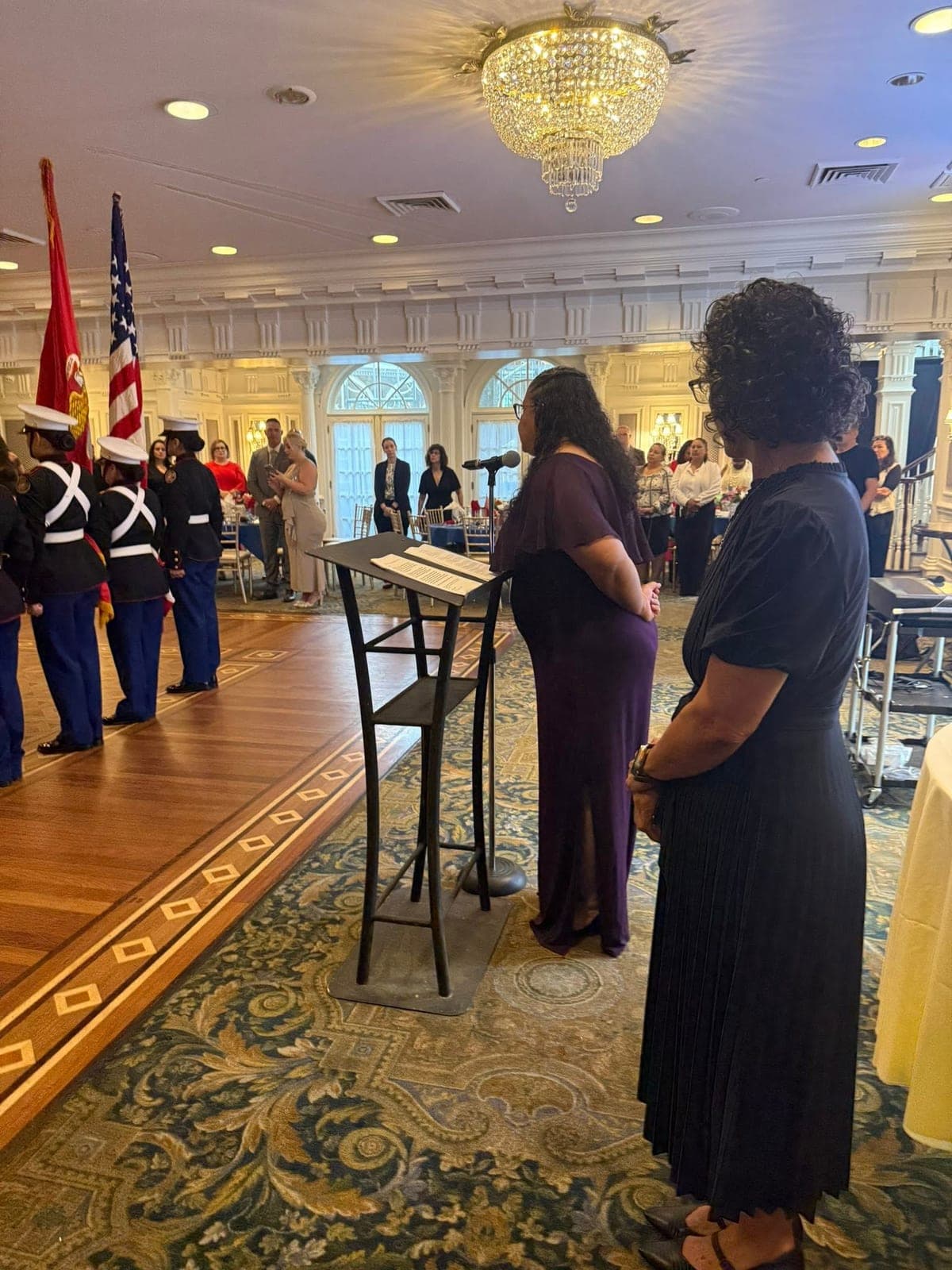 Two women at the podium as a Marine color guard stands by